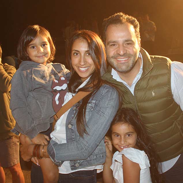 Family of two adults and two young kids smiling at the camera.